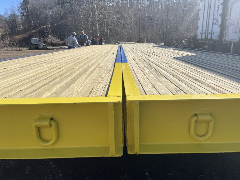 Portable timber bridge with yellow edges and wooden decking, showcasing construction details and workers in the background, emphasizing E&H Manufacturing's focus on innovative infrastructure solutions.