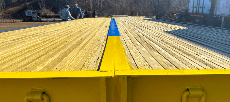 Stress-laminated timber bridge surface with yellow and blue accents, showcasing E&H Manufacturing's innovative design and construction for enhanced durability.