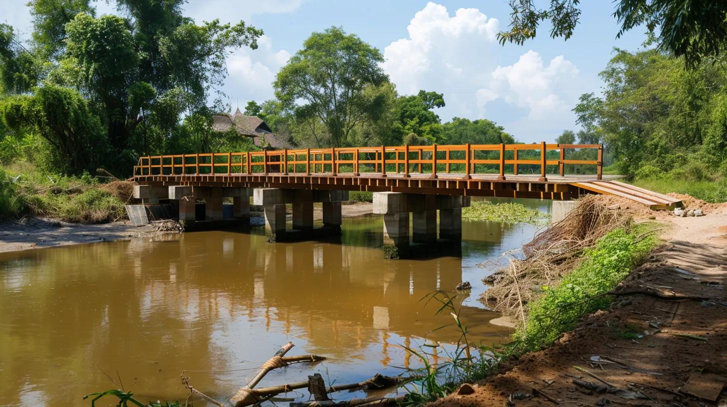 Wooden bridge over a river surrounded by lush greenery and blue sky with clouds.