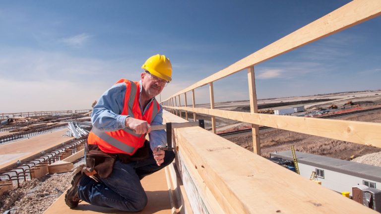 Construction worker in safety gear installing timber on a bridge, showcasing stress-laminated timber techniques in a construction setting.