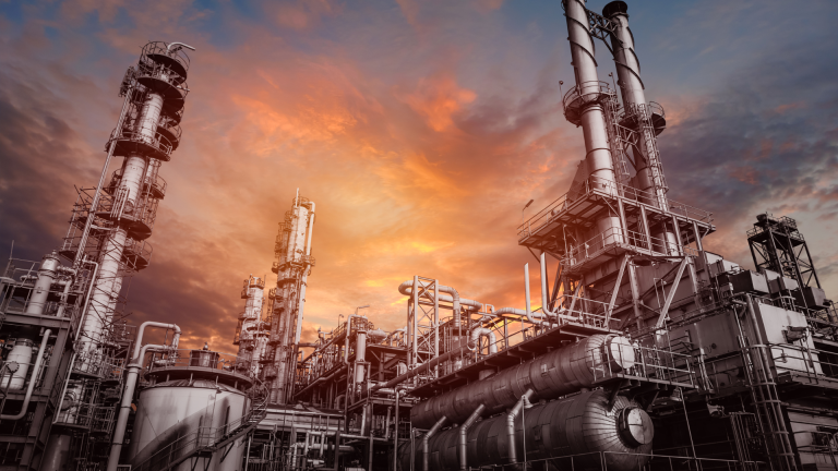 Industrial oilfield machinery against a dramatic sunset, showcasing complex structures and equipment essential for oil extraction and manufacturing processes.
