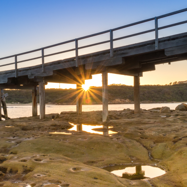 Timber bridge at sunset over rocky shoreline, highlighting sustainable infrastructure and engineering excellence in Charleston.